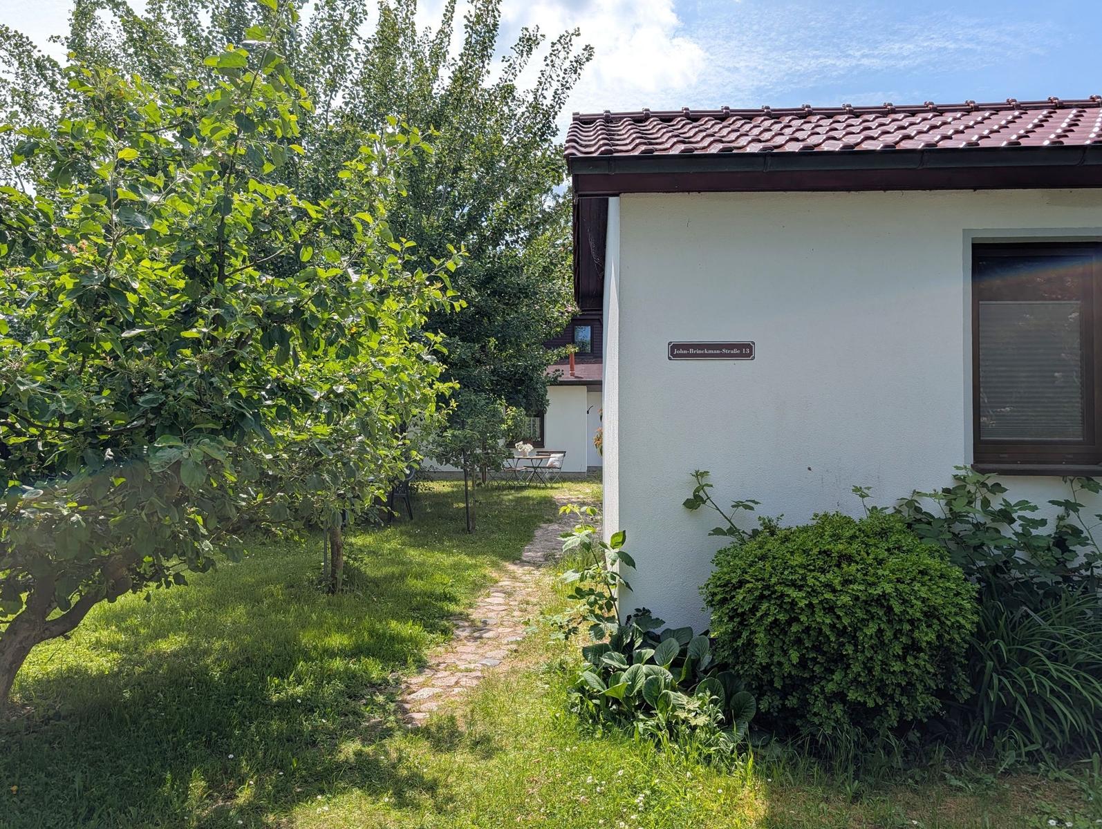 Haus mit Gartenweg, Bäumen und Straßenschild John-Brinekman-Straße 13.