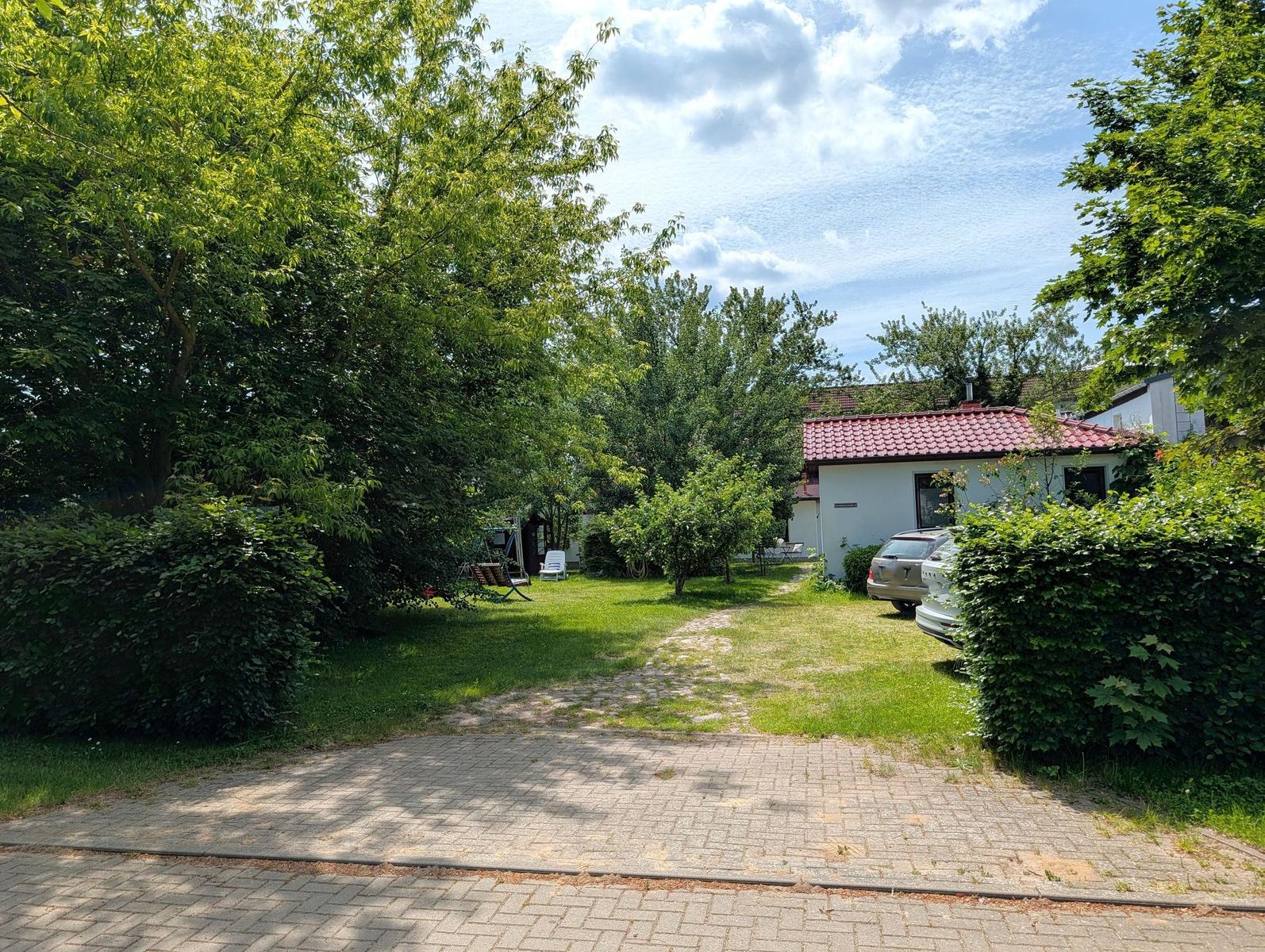 Hinterhof mit Rasen, Bäumen und einem weißen Haus mit rotem Dach.