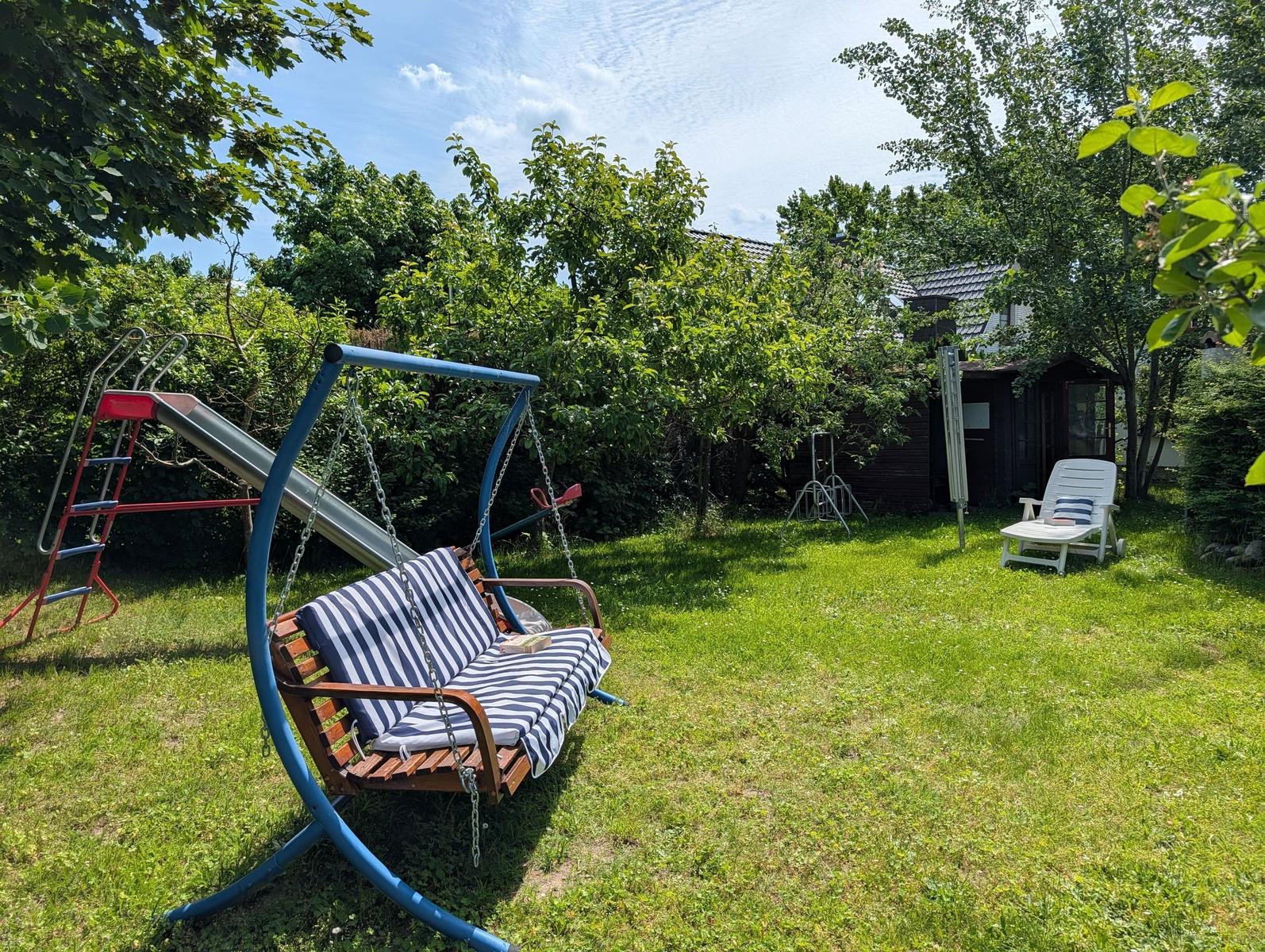 Hinterhof mit Schaukel, Spielplatz und Liegestuhl auf Gras.