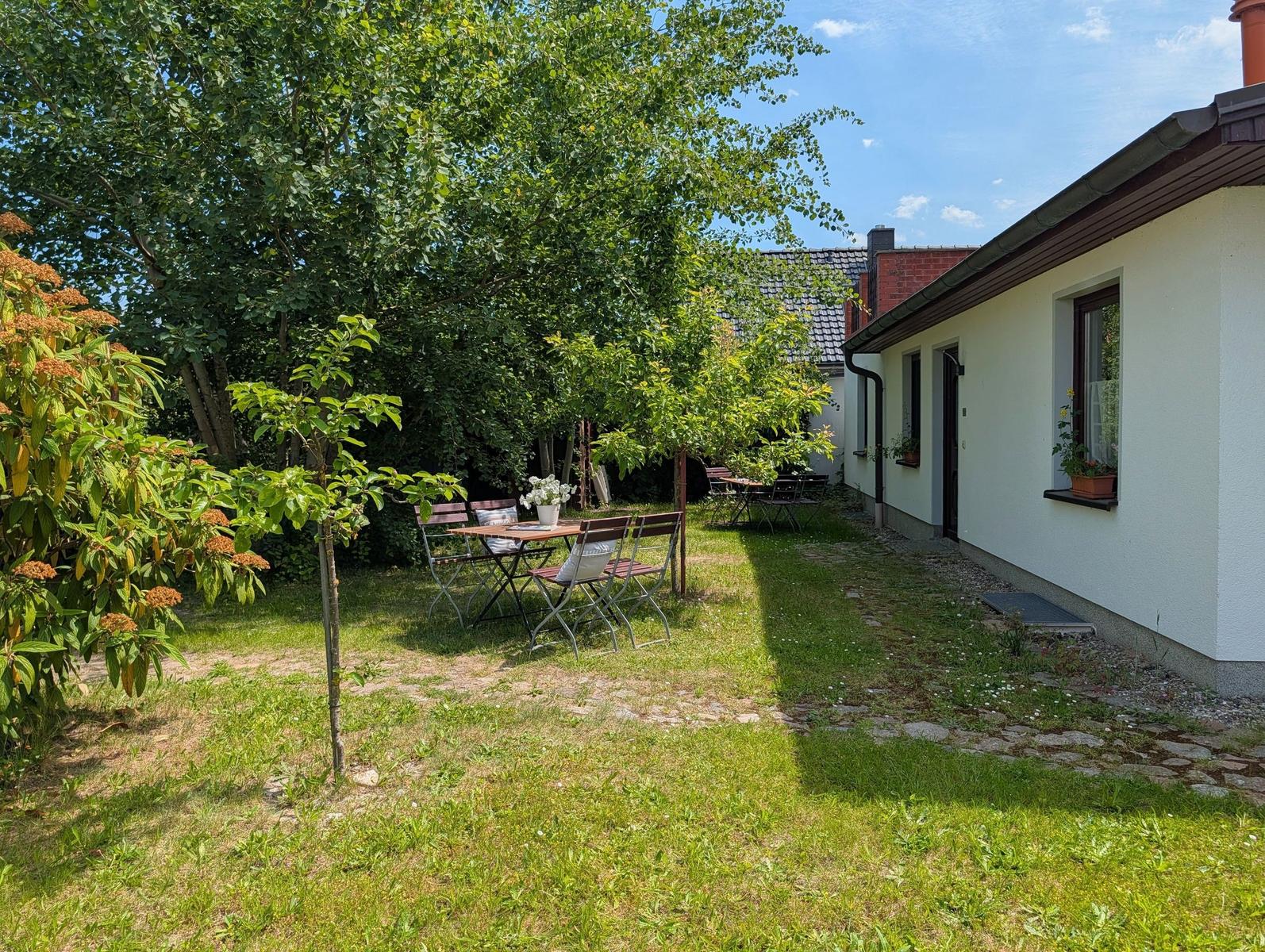 Hinterhof mit Tisch, Stühlen und Pflanzen neben einem weißen Haus.