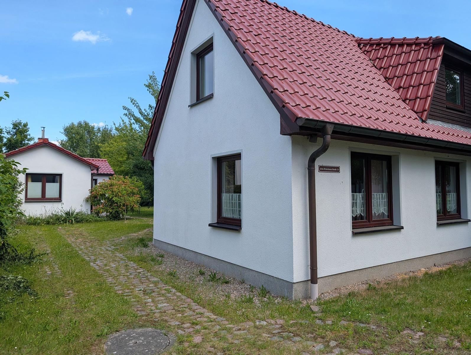 Wohnhaus mit rotem Dach und weißen Wänden, gepflasterte Zugangsweg und grüner Garten.
