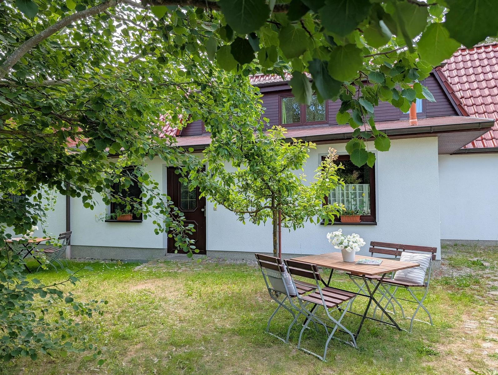 Haus mit Garten, Tisch und Stühlen unter Bäumen. Fenster mit Blumenkästen.