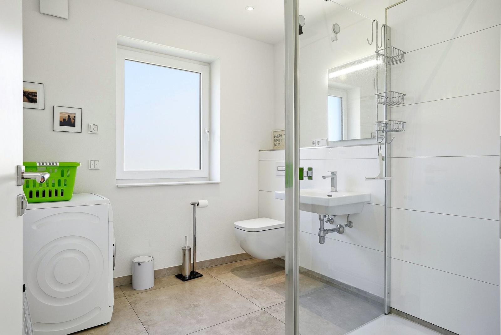Bathroom with shower, sink, and toilet. Window, washing machine, and sink visible.