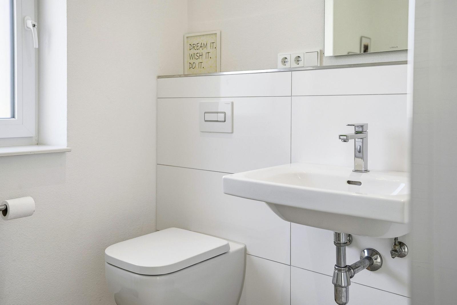 Bathroom with toilet, sink, and mirror. Window provides natural light.