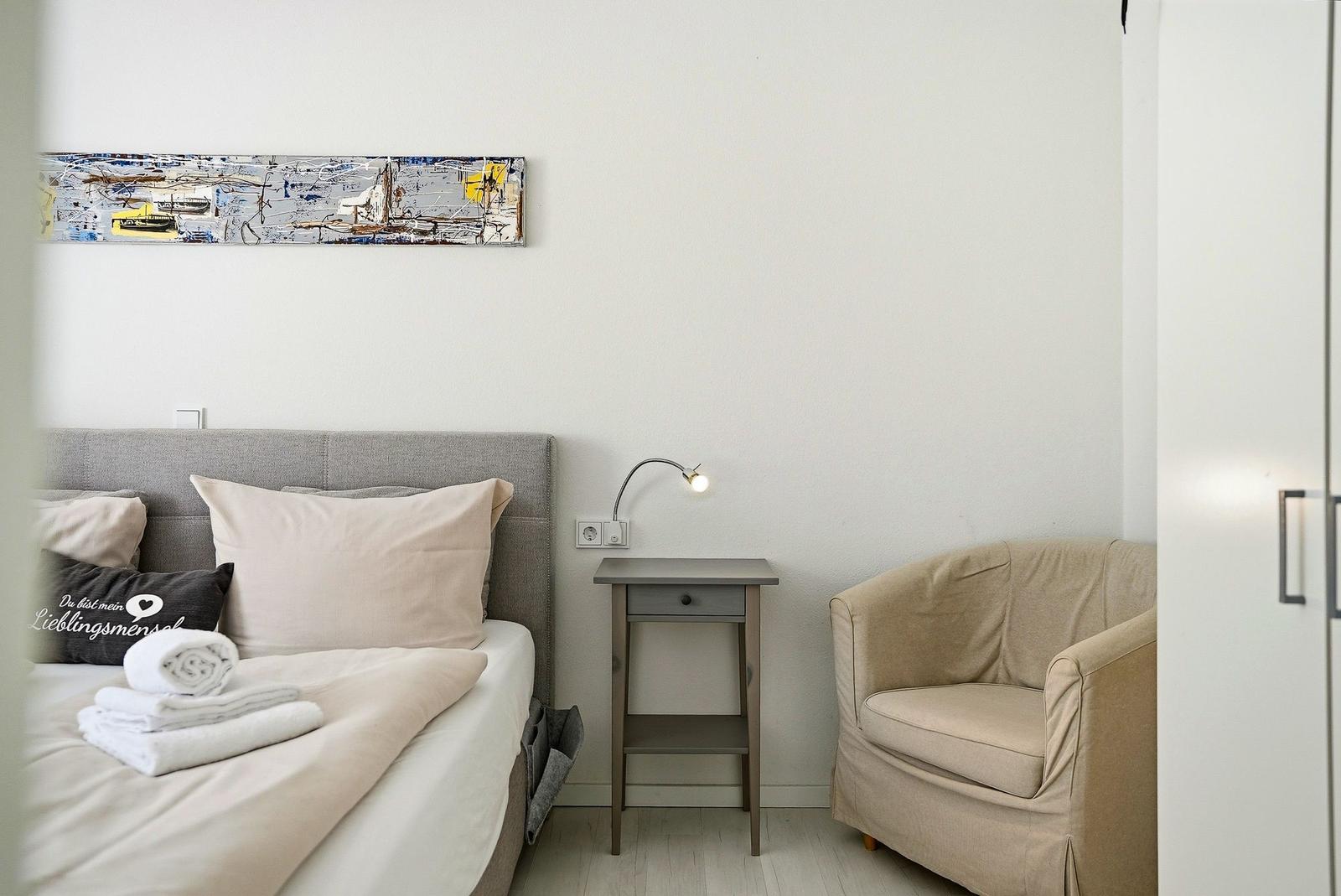 Bedroom with bed, armchair, and nightstand. Wall art above the bed.