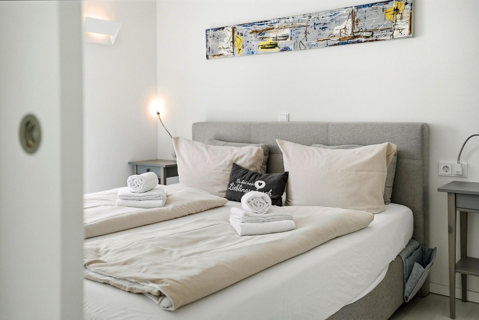 A bed with bedding, pillows, and towels. A painting hangs on the wall.