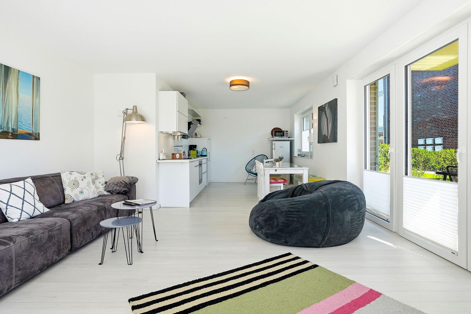 Apartment with sofa, dining area, and balcony. White walls and floor. Large bean bag.