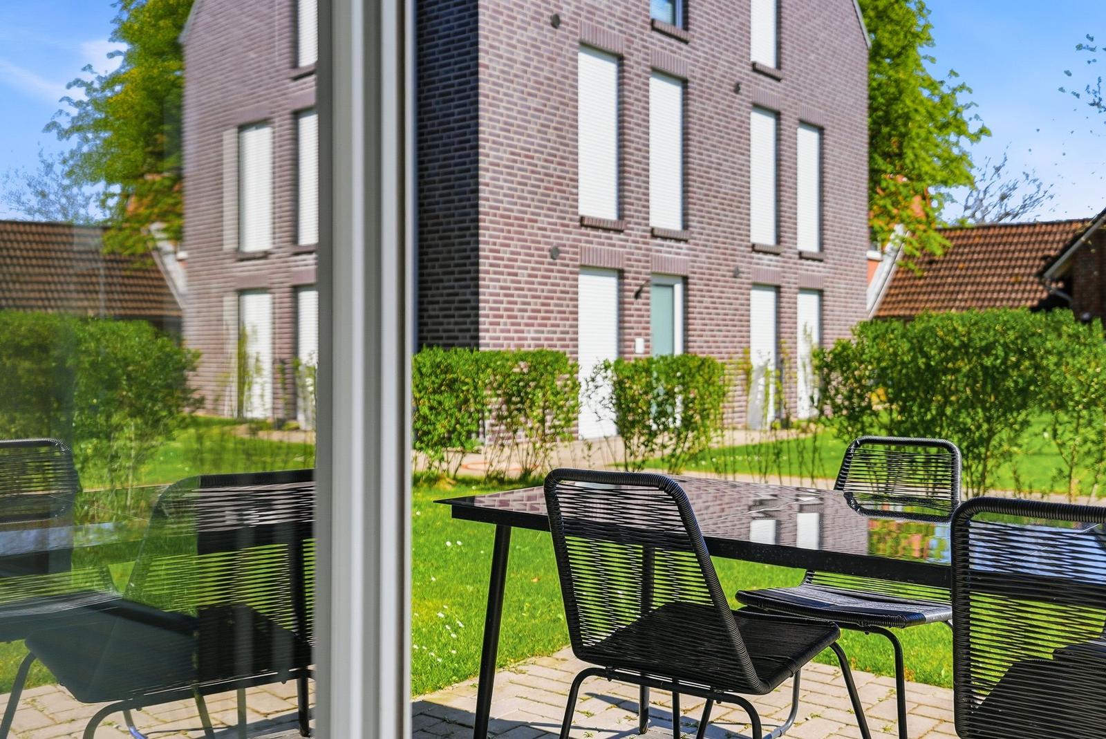 Terrace with table and chairs. View of green lawn and brick house.