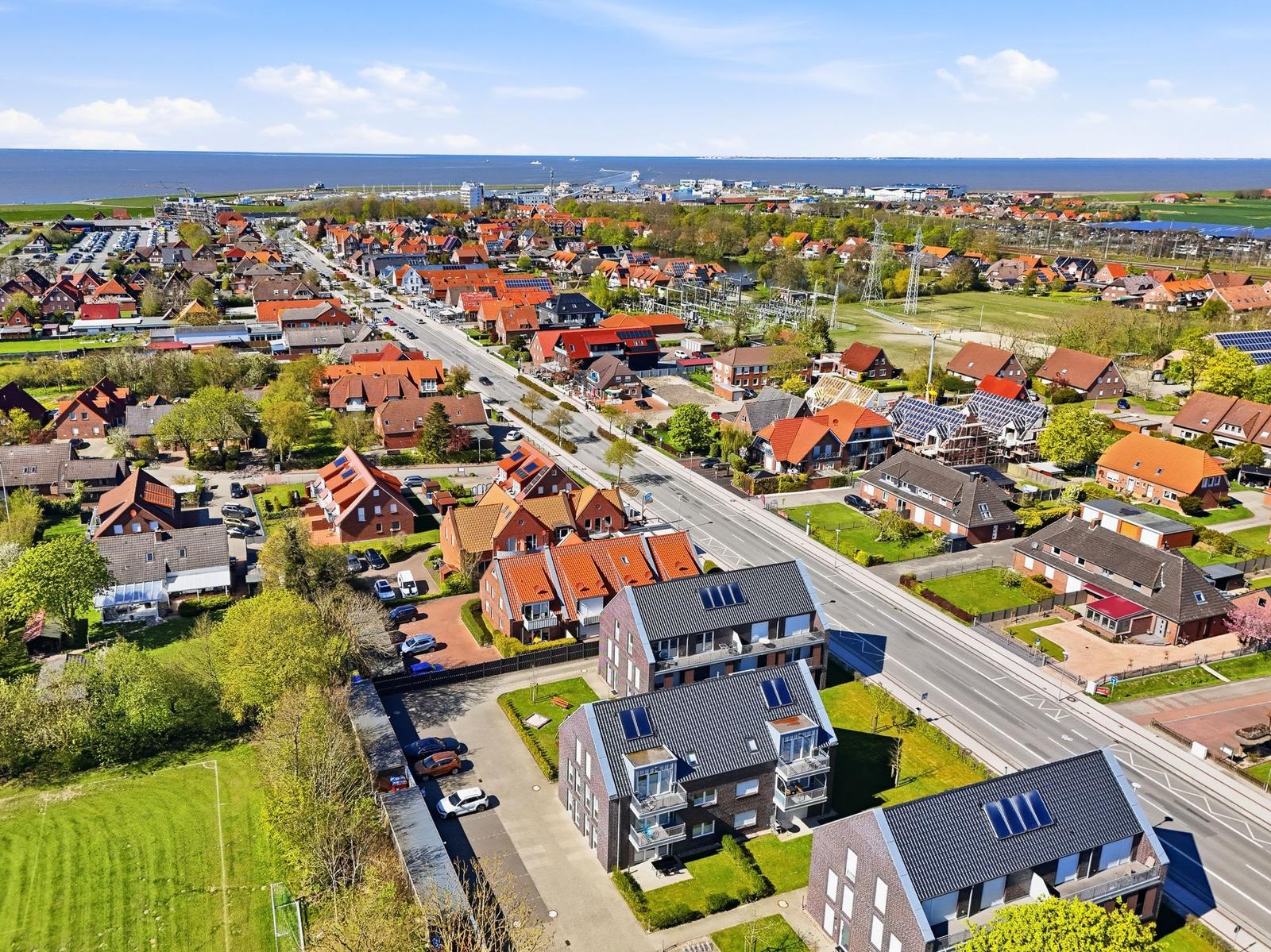Aerial view of a residential area near the sea with houses, roads, and green spaces.