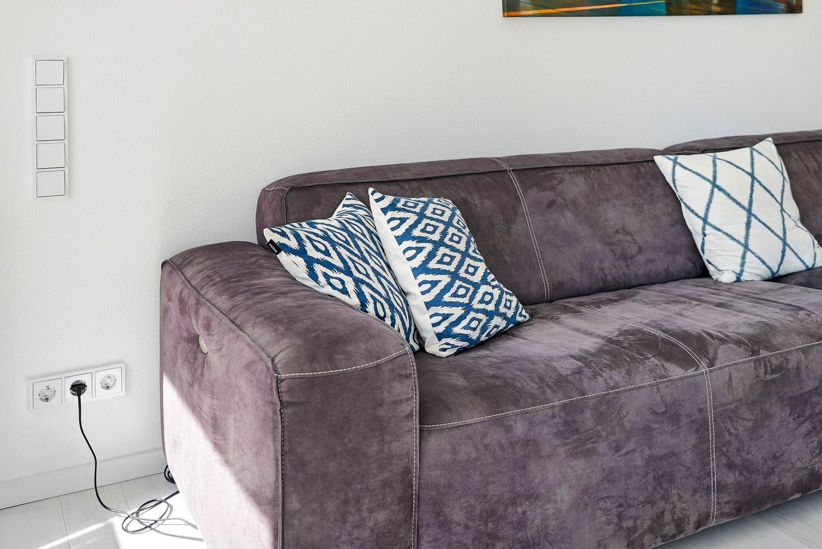 A gray sofa with blue cushions and white stitching against the wall.