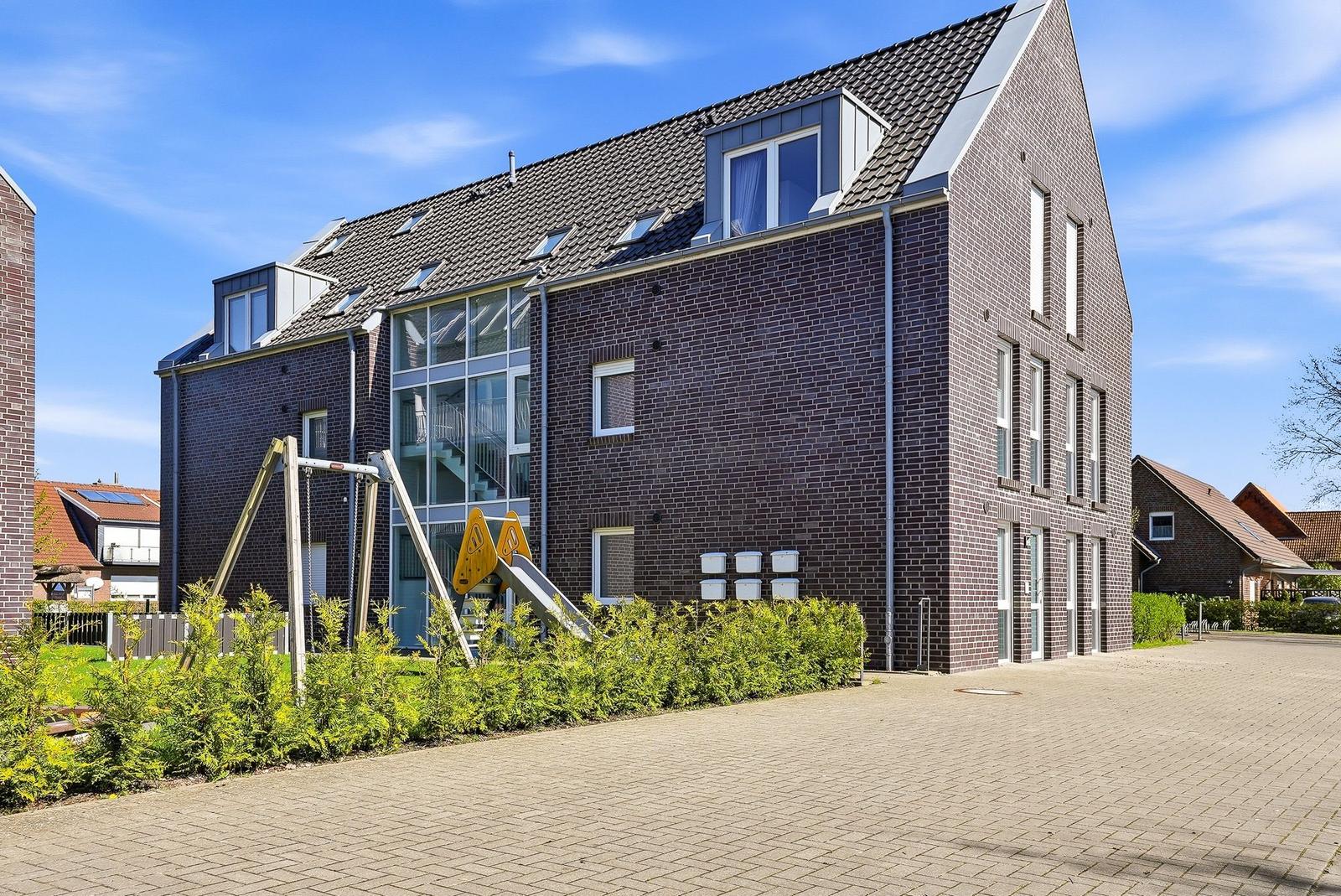 Modern multi-family house with playground and paved forecourt.
