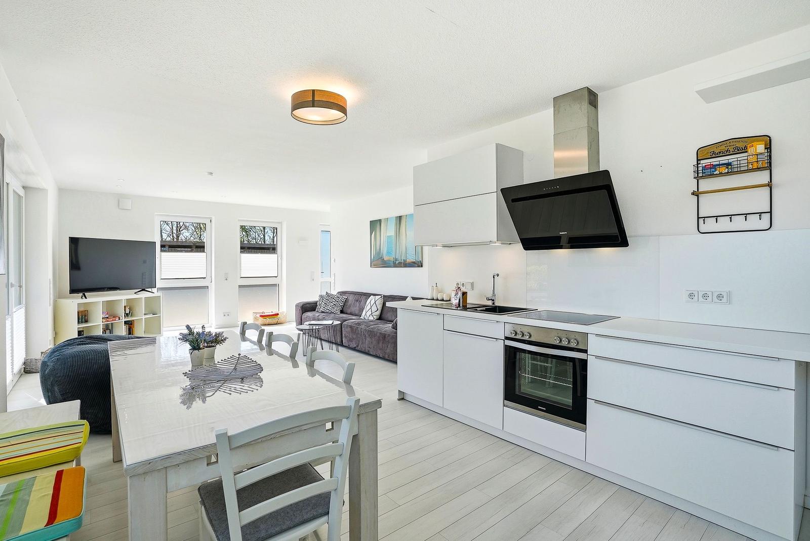Kitchen with dining area, living room and TV. White built-in kitchen with stainless steel appliances.