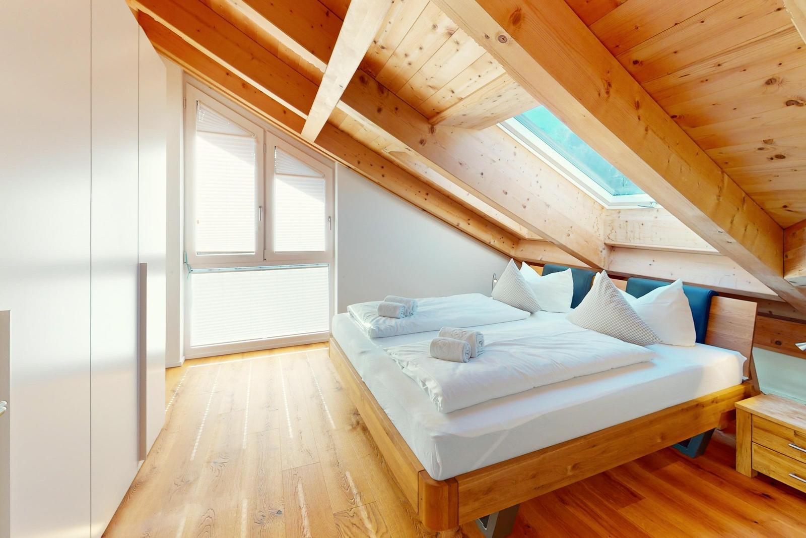 Schlafzimmer mit Holzboden, Dachschrägen und Dachfenster. Bett mit weißen Laken und Kissen.