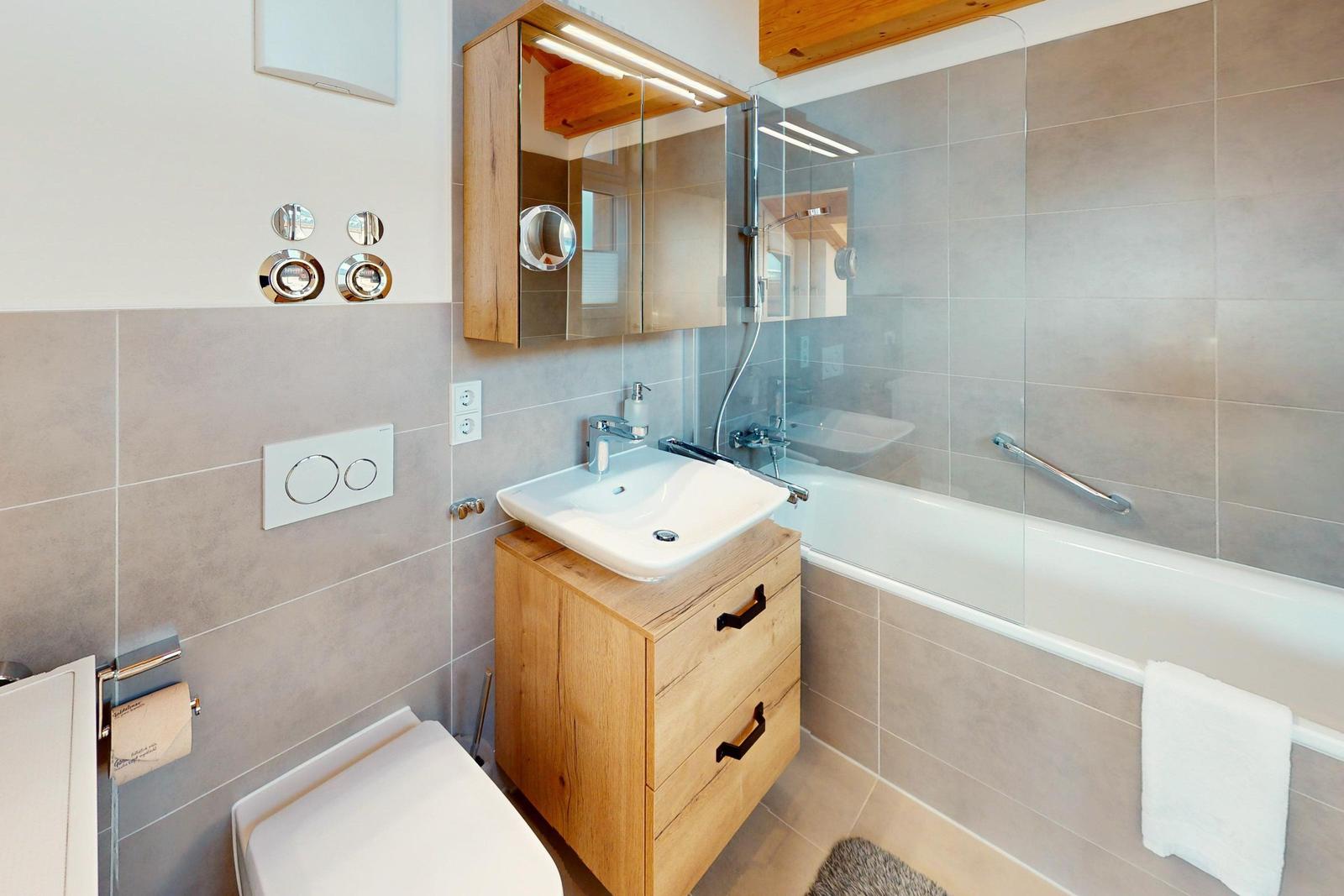 Badezimmer mit Badewanne, Waschbecken und Toilette. Holzregal und Glaswand.