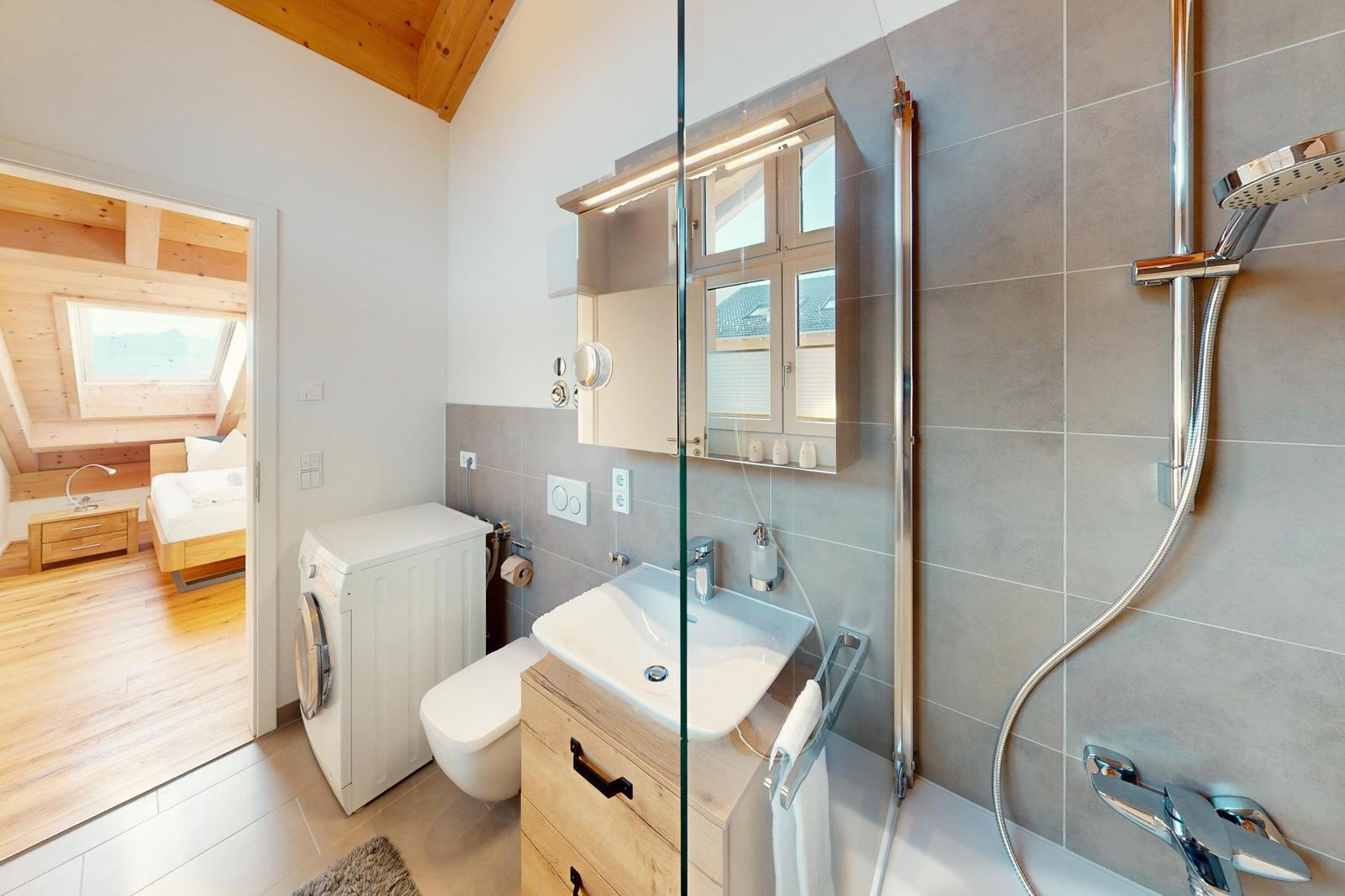Badezimmer mit Dusche, Waschmaschine und Blick in Schlafzimmer