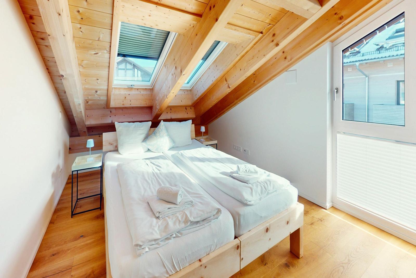 Schlafzimmer mit Doppelbett, Holzdecke und Fenstern.