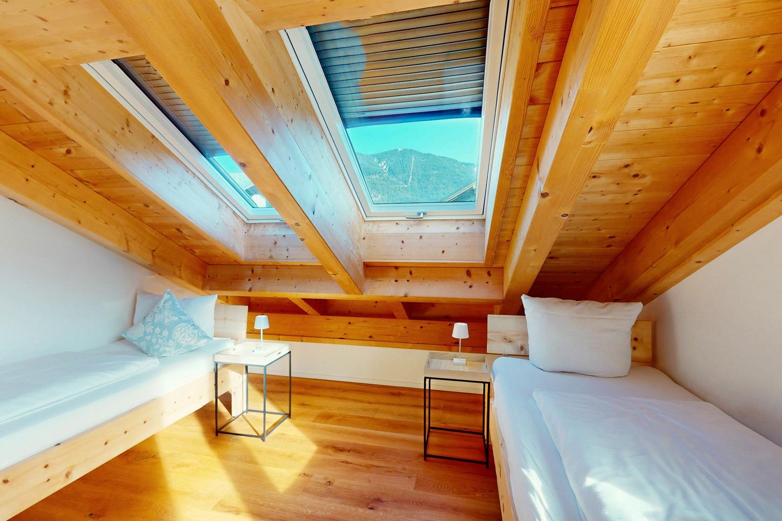 Zwei Betten unter Dachschrägen mit Holzdecke und Dachfenster. Blick auf Berge.