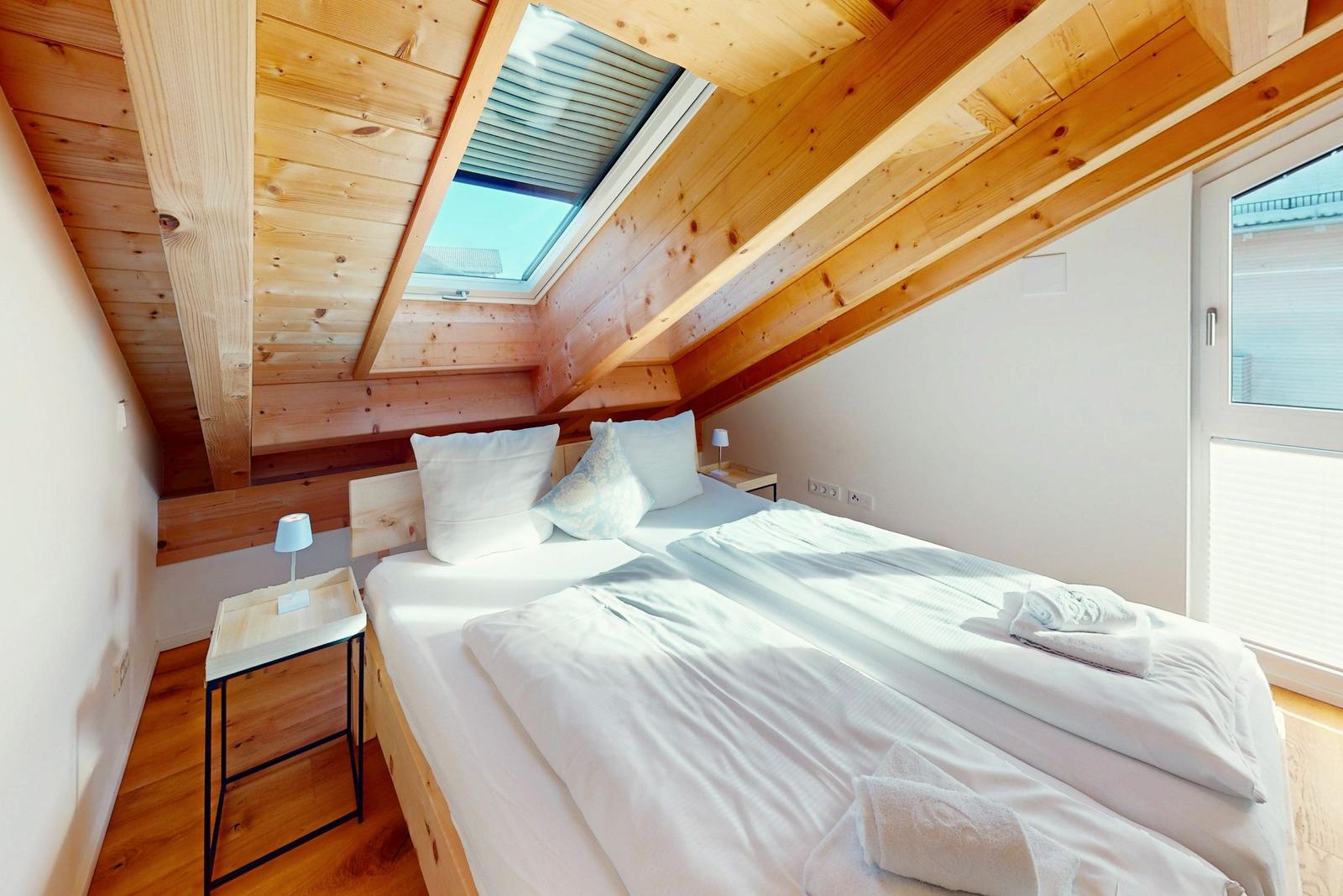 Schlafzimmer mit Dachschrägen, Holzdecke, Dachfenster und Bett mit weißen Bettwäsche.