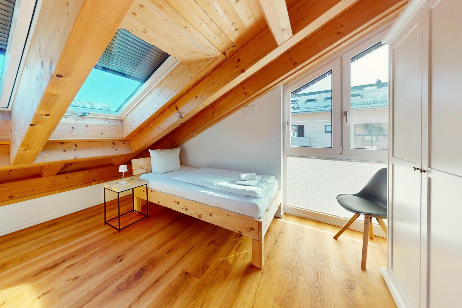 Ein Schlafzimmer mit Dachschrägen, Holzboden und einem Bett unter Dachschrägen.