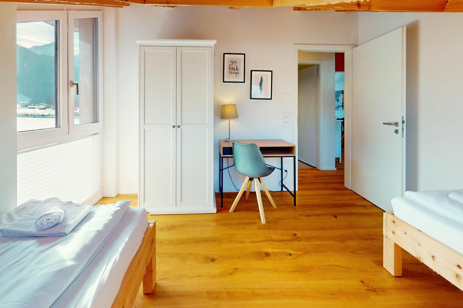 Zimmer mit zwei Betten, Schreibtisch und Blick auf Berge.