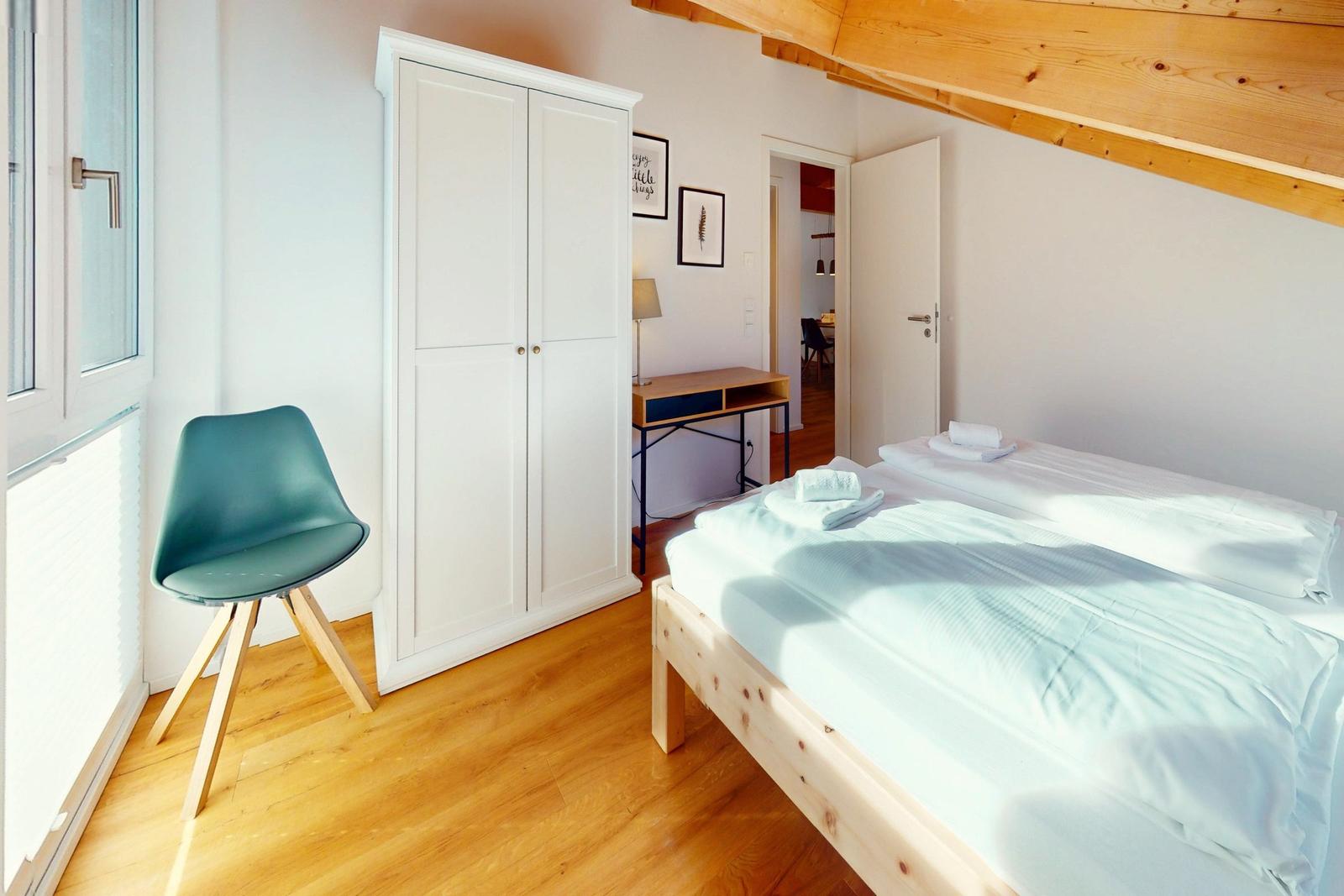 Schlafzimmer mit Bett, Schreibtisch und Kleiderschrank unter Holzdecke.