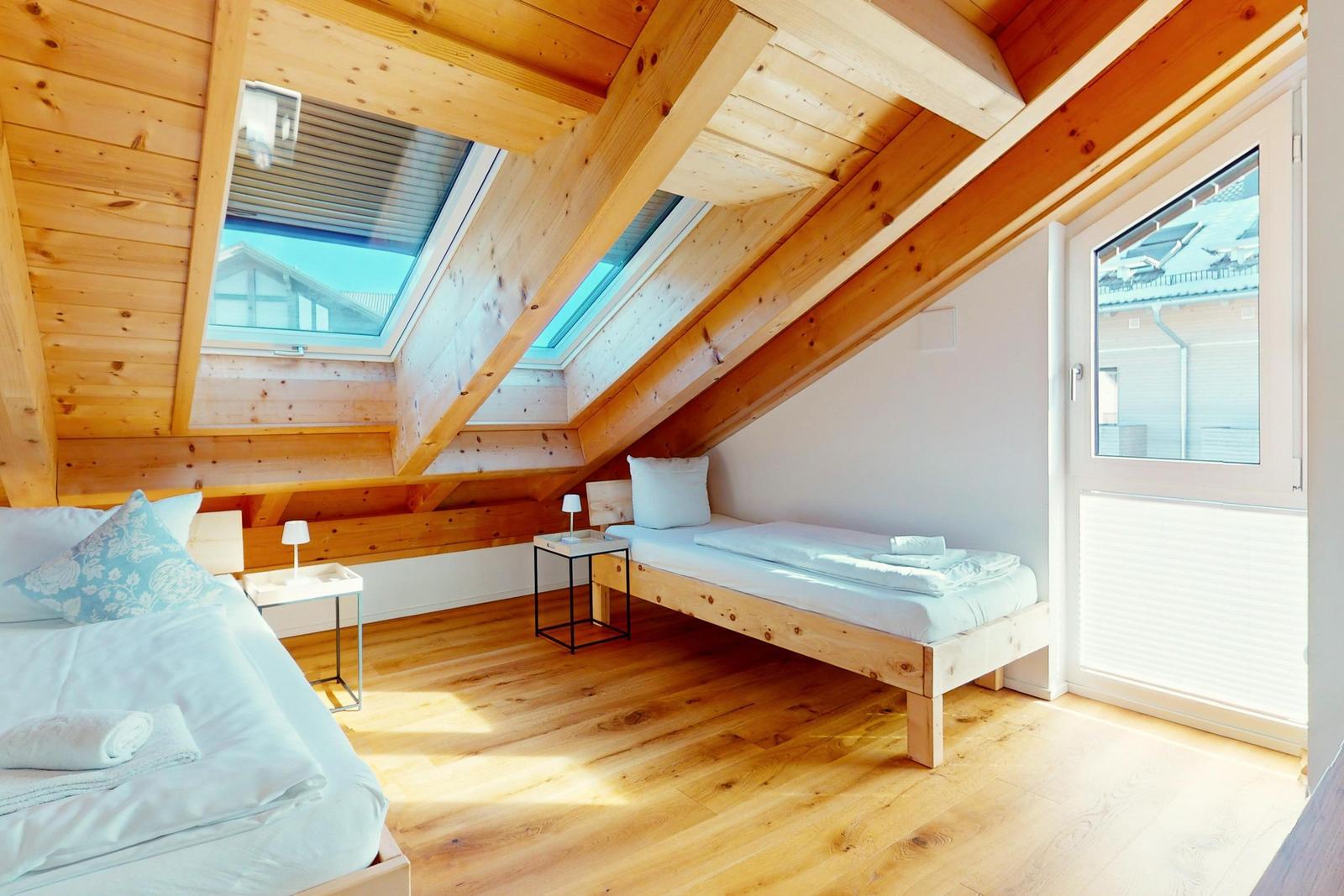 Schlafzimmer mit Dachschrägen, Holzboden und zwei Betten. Fenster und Dachfenster.