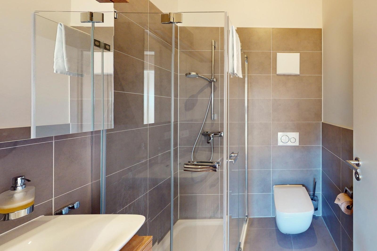 Dusche mit Glaswand, Waschbecken und Toilette in moderner Ausstattung.