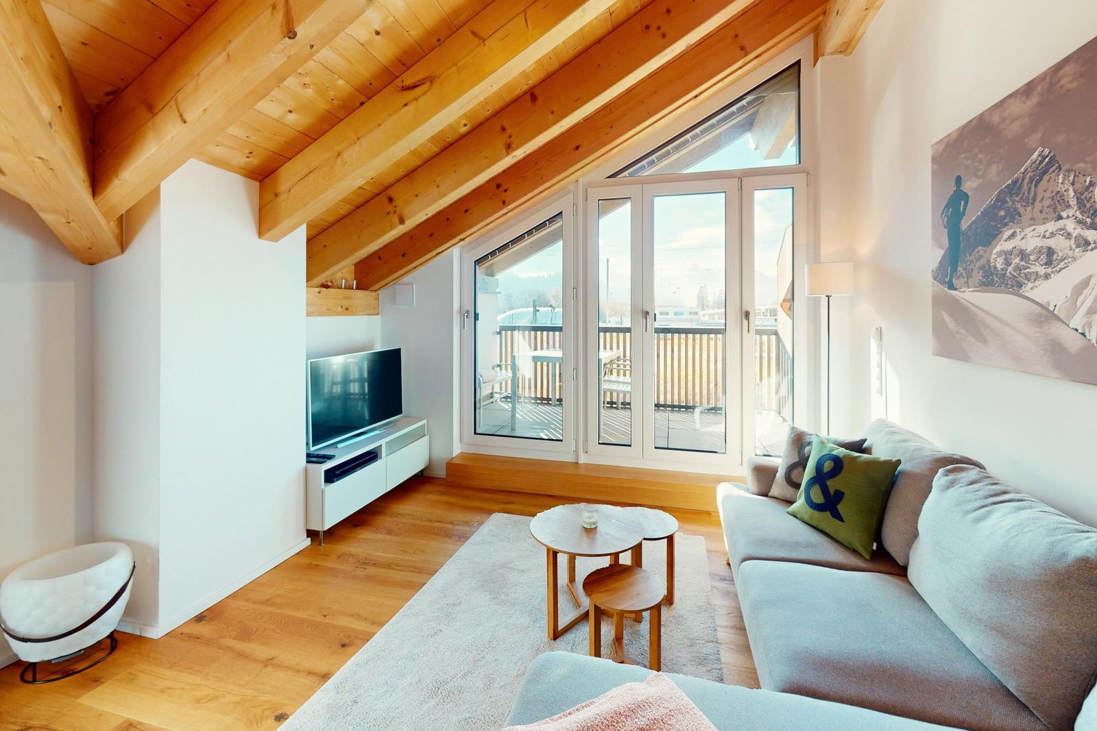 Wohnzimmer mit Holzdecke, Sofa, TV und Balkonansicht.