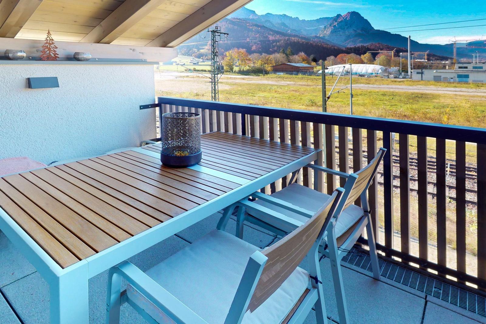 Terrasse mit Tisch und Stühlen, Blick auf Berge und Bahngleise.