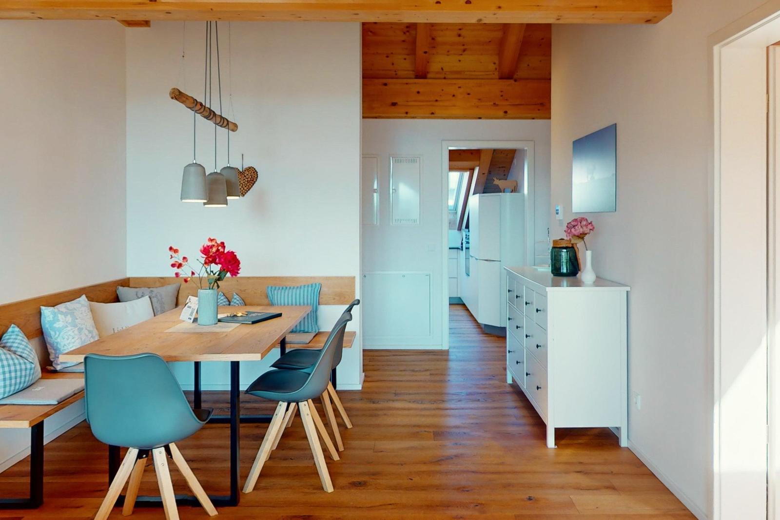 Essbereich mit Sitzbank, Tisch und Stühlen. Holzdecke und Boden. Küche im Hintergrund.