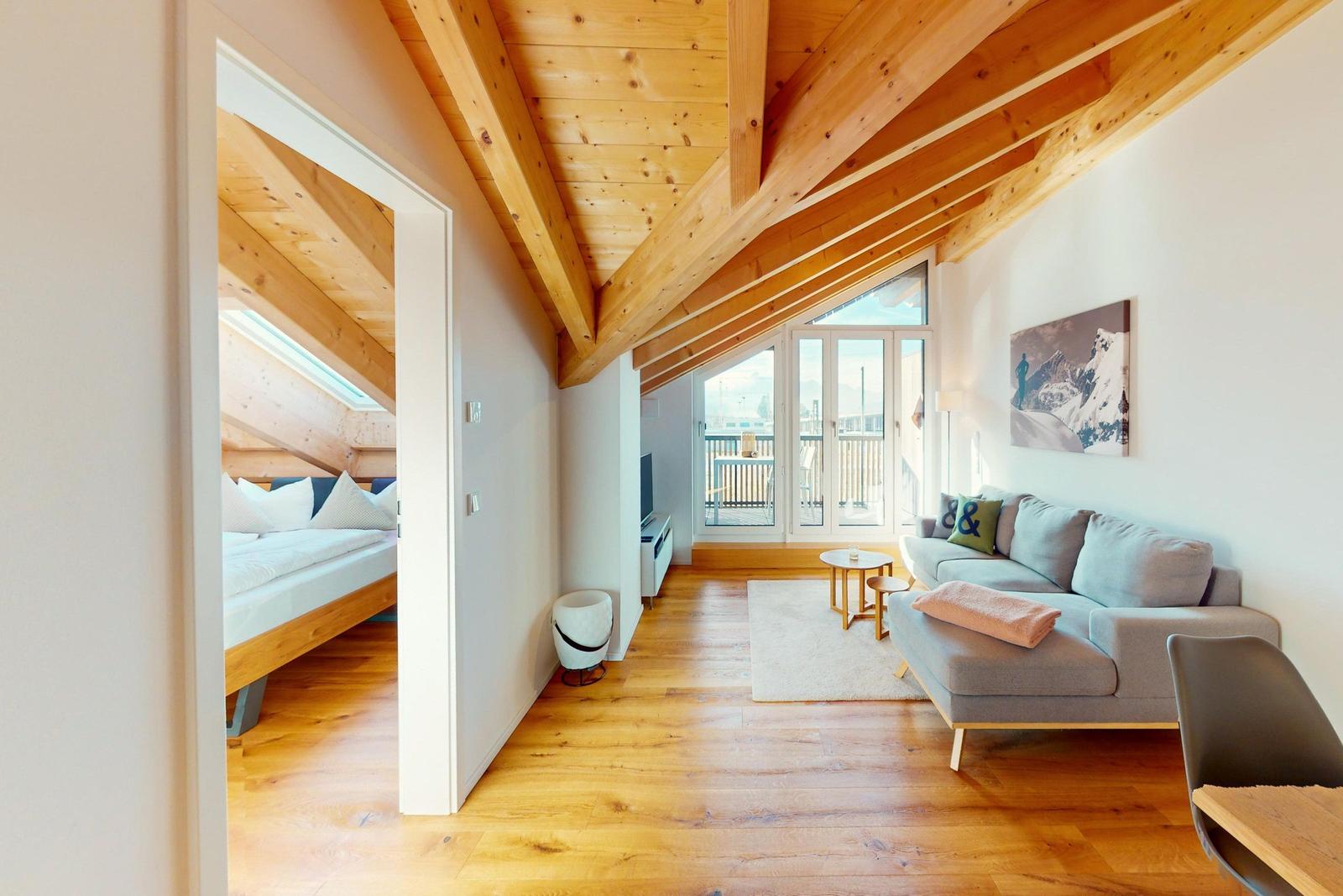 Wohnbereich mit Sofa, Balkon und Schlafzimmer mit Dachschrägen.