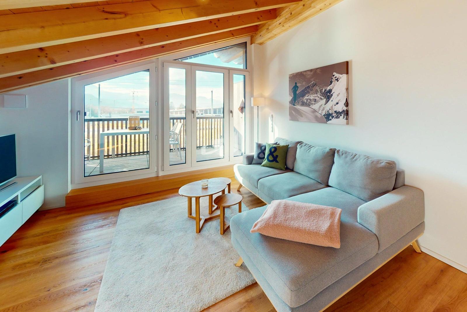 Wohnzimmer mit Sofa, Couchtisch und Balkon. Holzdecke und Boden.