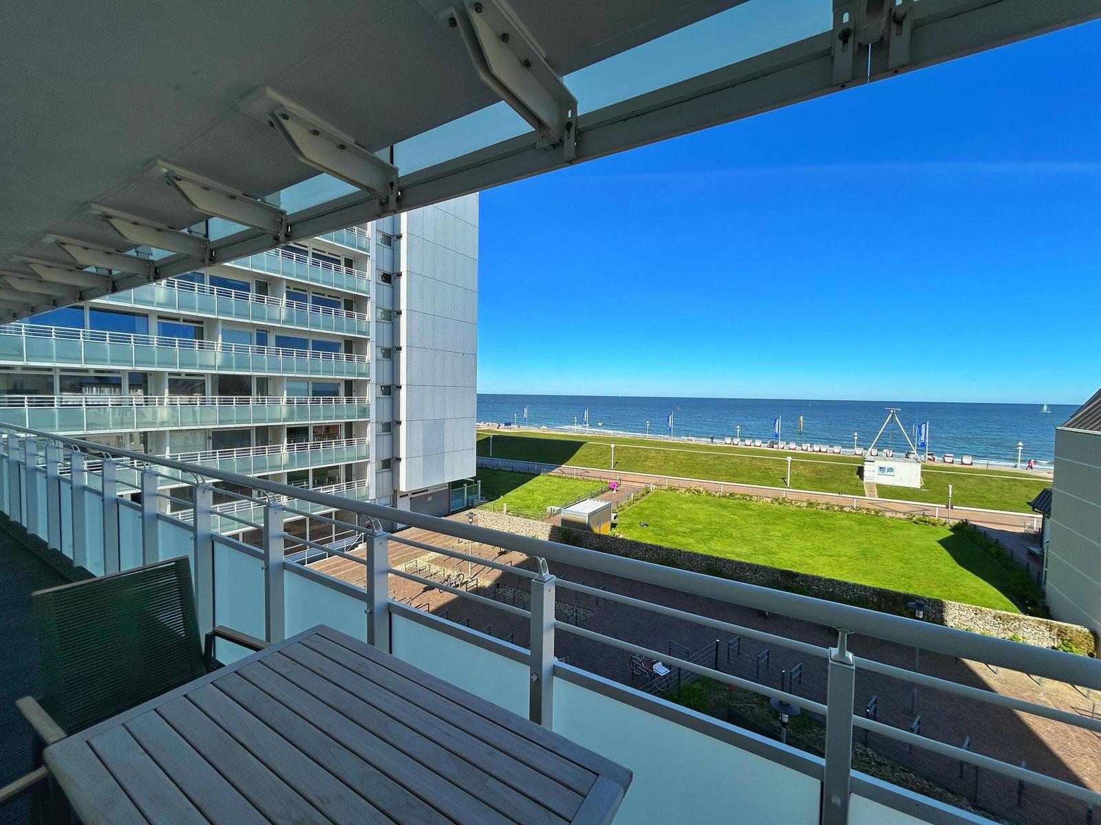 Terrasse mit Tisch und Stuhl bietet Blick auf Meer und Grünfläche.