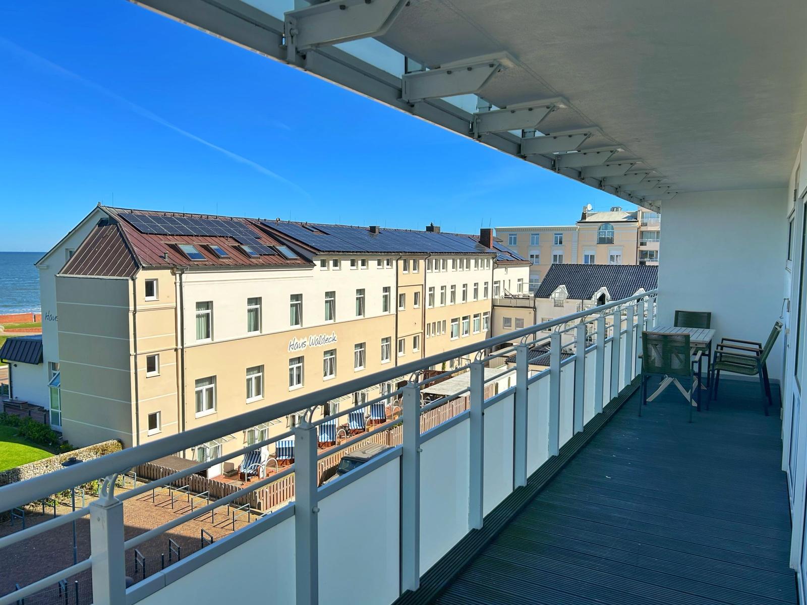 Terrasse mit Tisch und Stühlen, Blick auf Haus Waldeck und Meer.