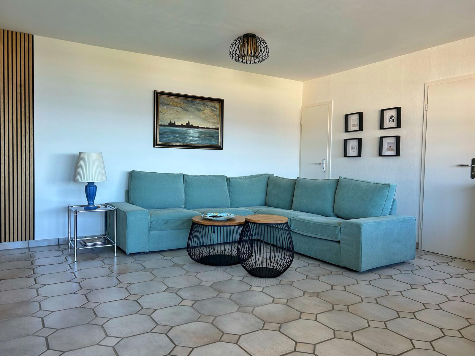 Wohnzimmer mit blauem Sofa, zwei runden Tischen und hexagonalen Bodenfliesen.