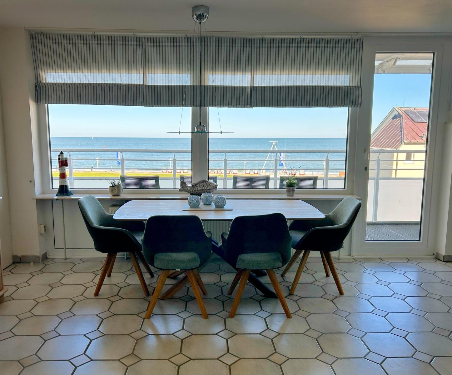 Esszimmer mit Blick aufs Meer und Balkon. Holztisch, Stühle und Fensterfront.