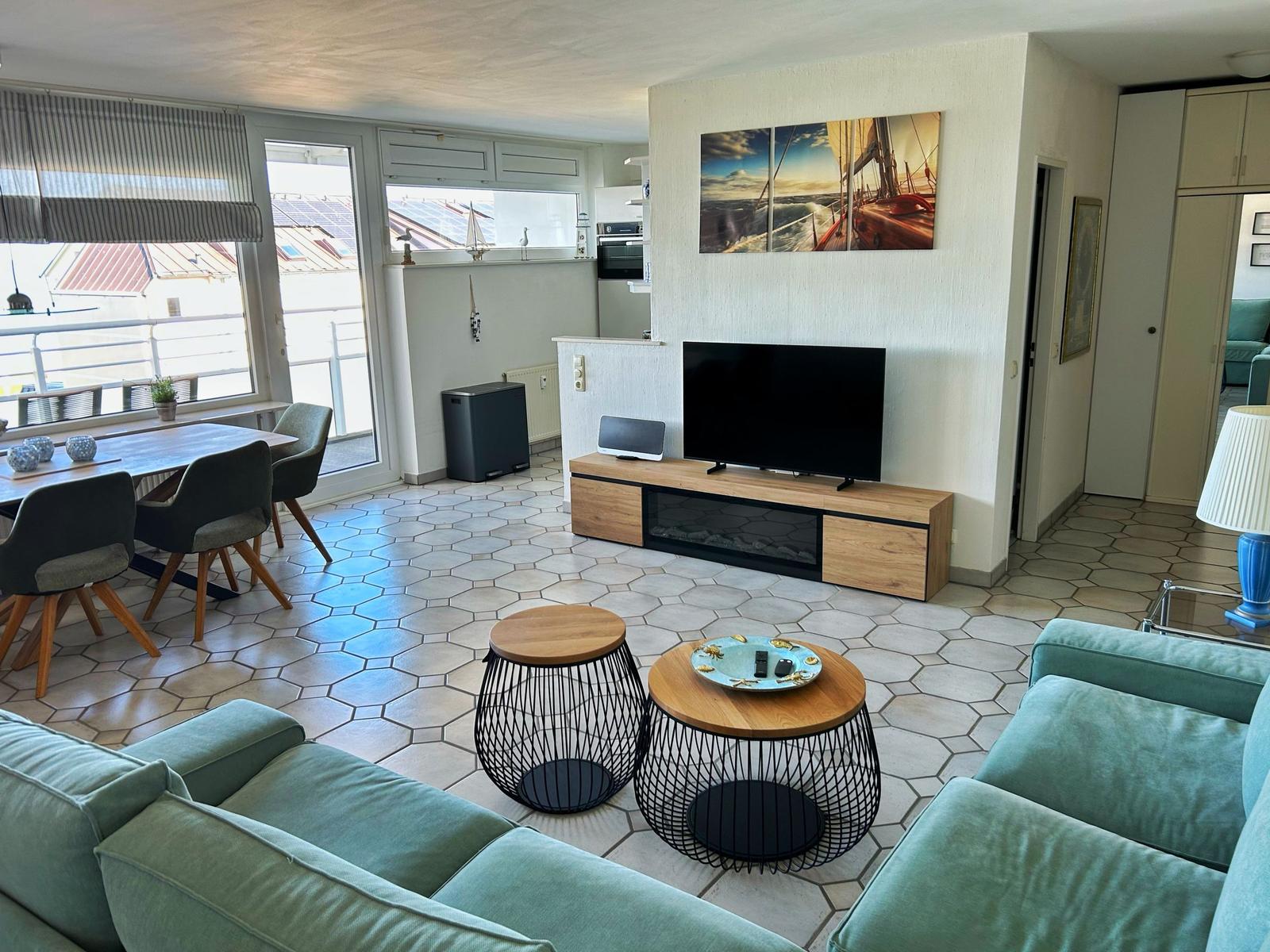 Wohnzimmer mit Sofa, TV und Essbereich. Balkon und Küchenbereich sichtbar.
