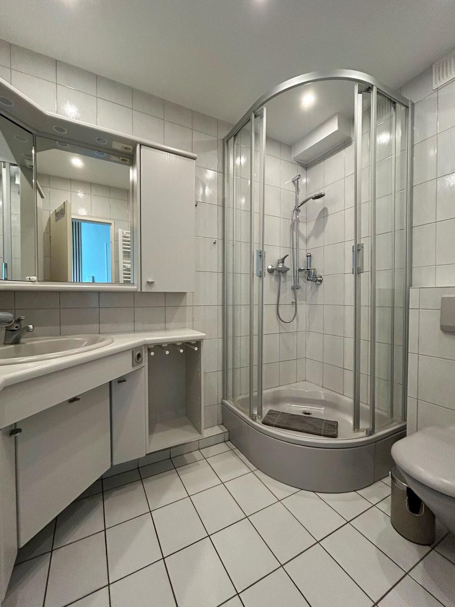 Badezimmer mit Dusche, Waschbecken und Toilette. Fliesen und Spiegel sichtbar.