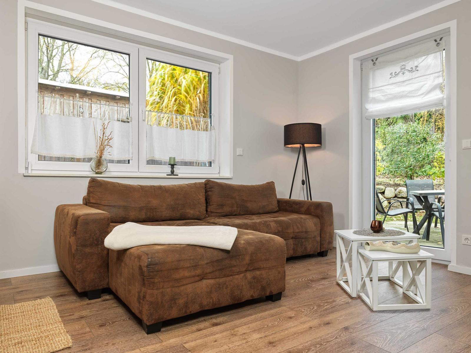 Ein Wohnzimmer mit braunem Sofa, Holzboden und Blick auf Garten.