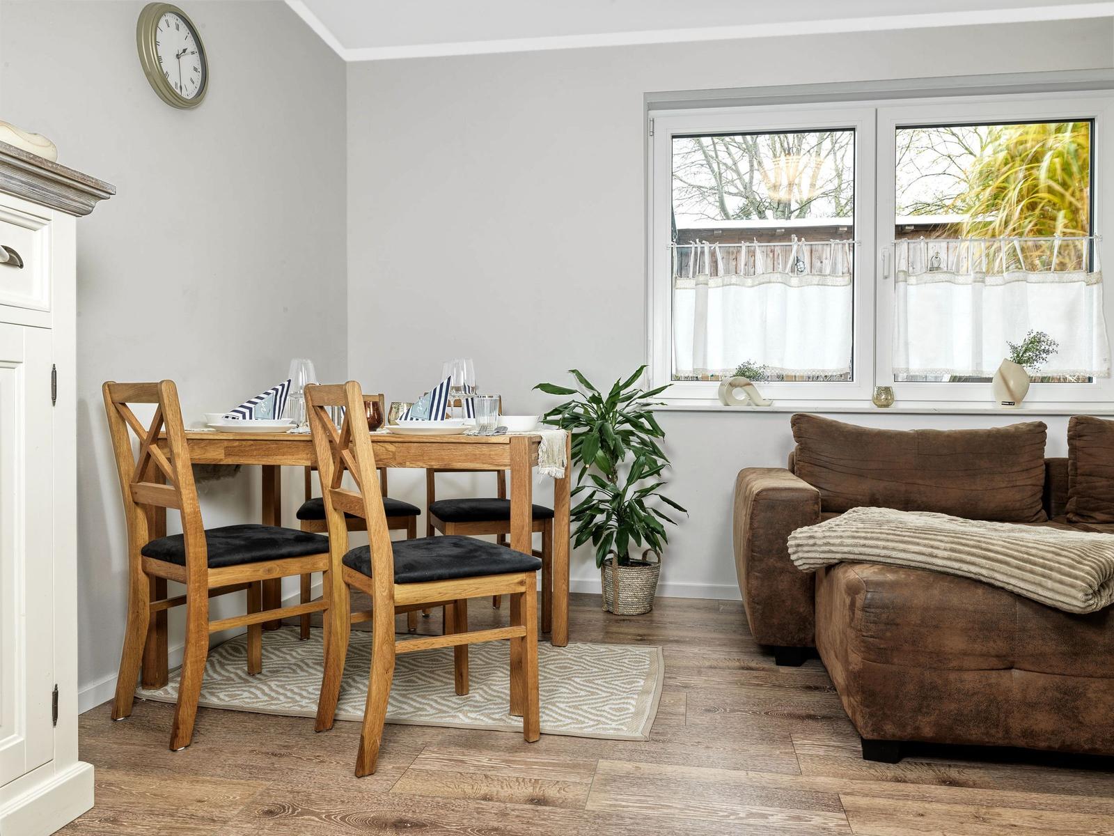 Essbereich mit Holztisch und Stühlen. Neben dem Fenster steht ein brauner Sofa.