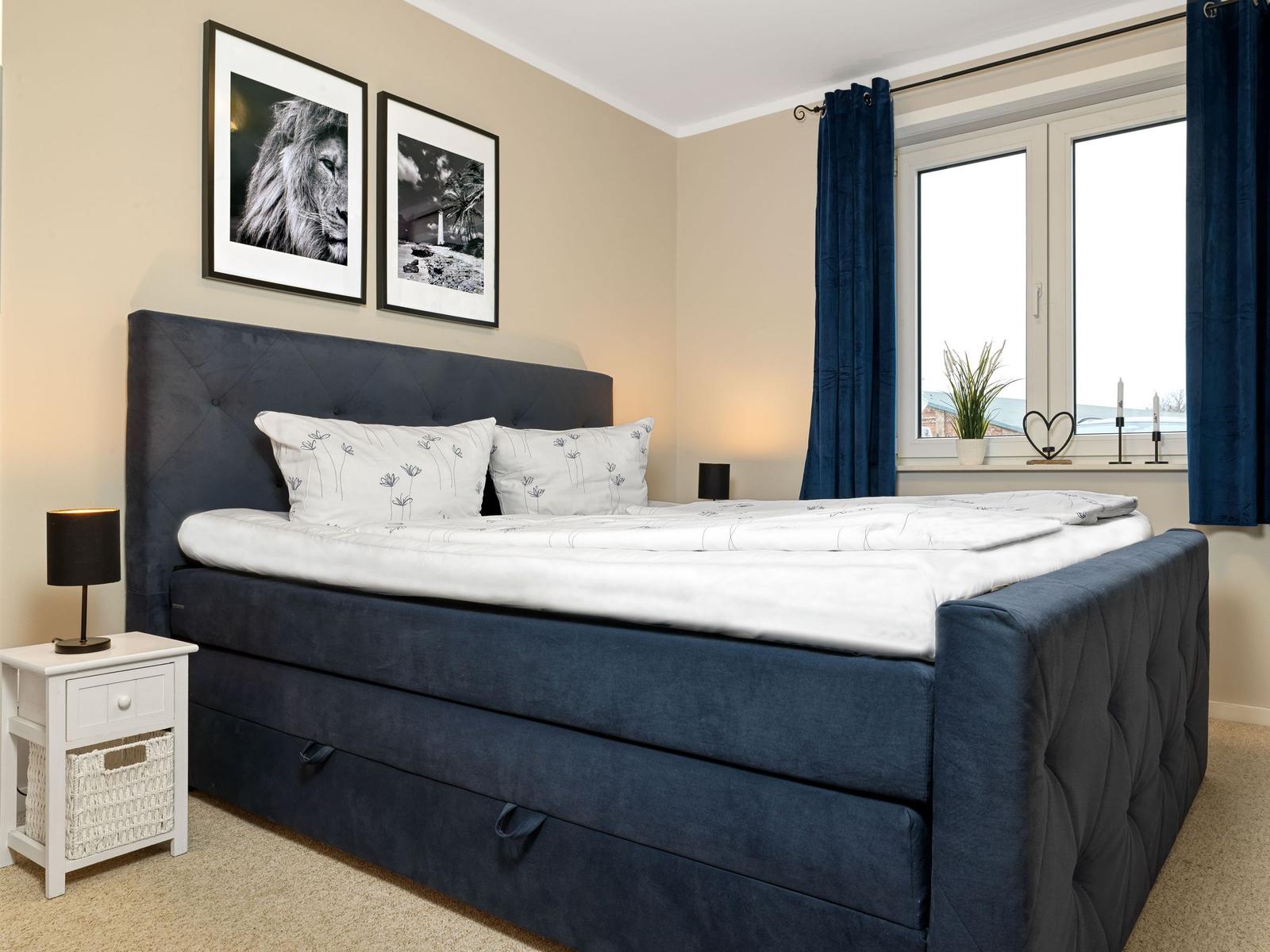 Schlafzimmer mit Bett, Nachttisch und Fenster mit Vorhängen.