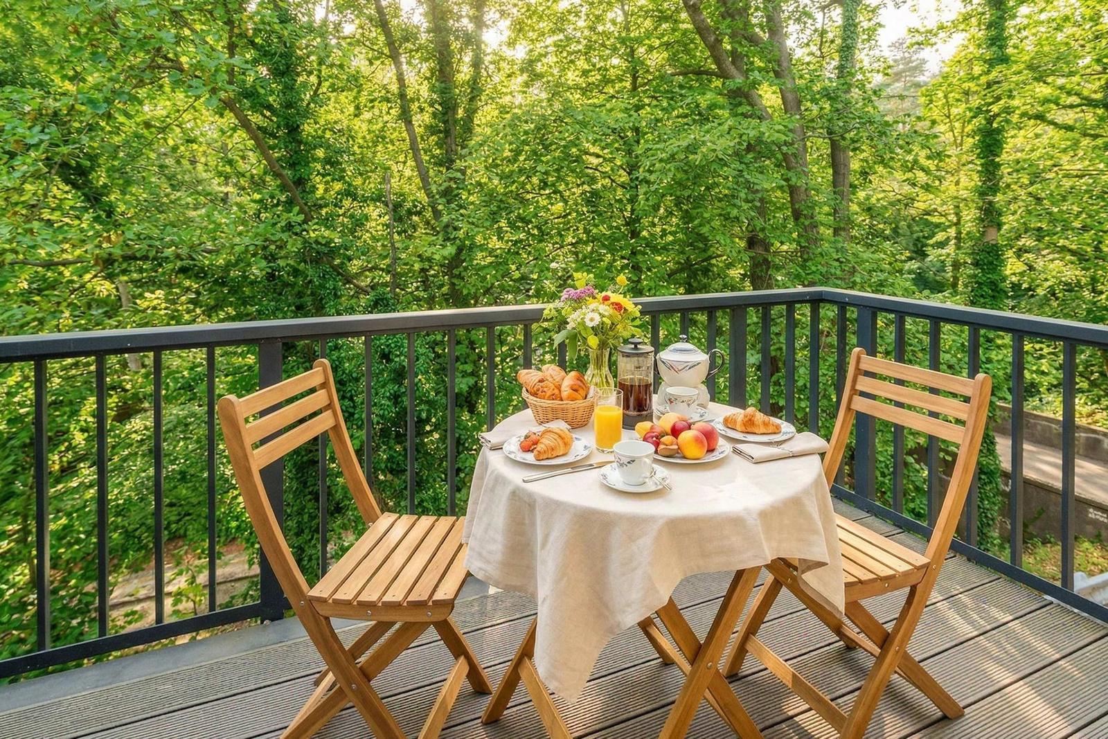 Terrasse mit Tisch, Stühlen und Frühstück, umgeben von grünen Bäumen.