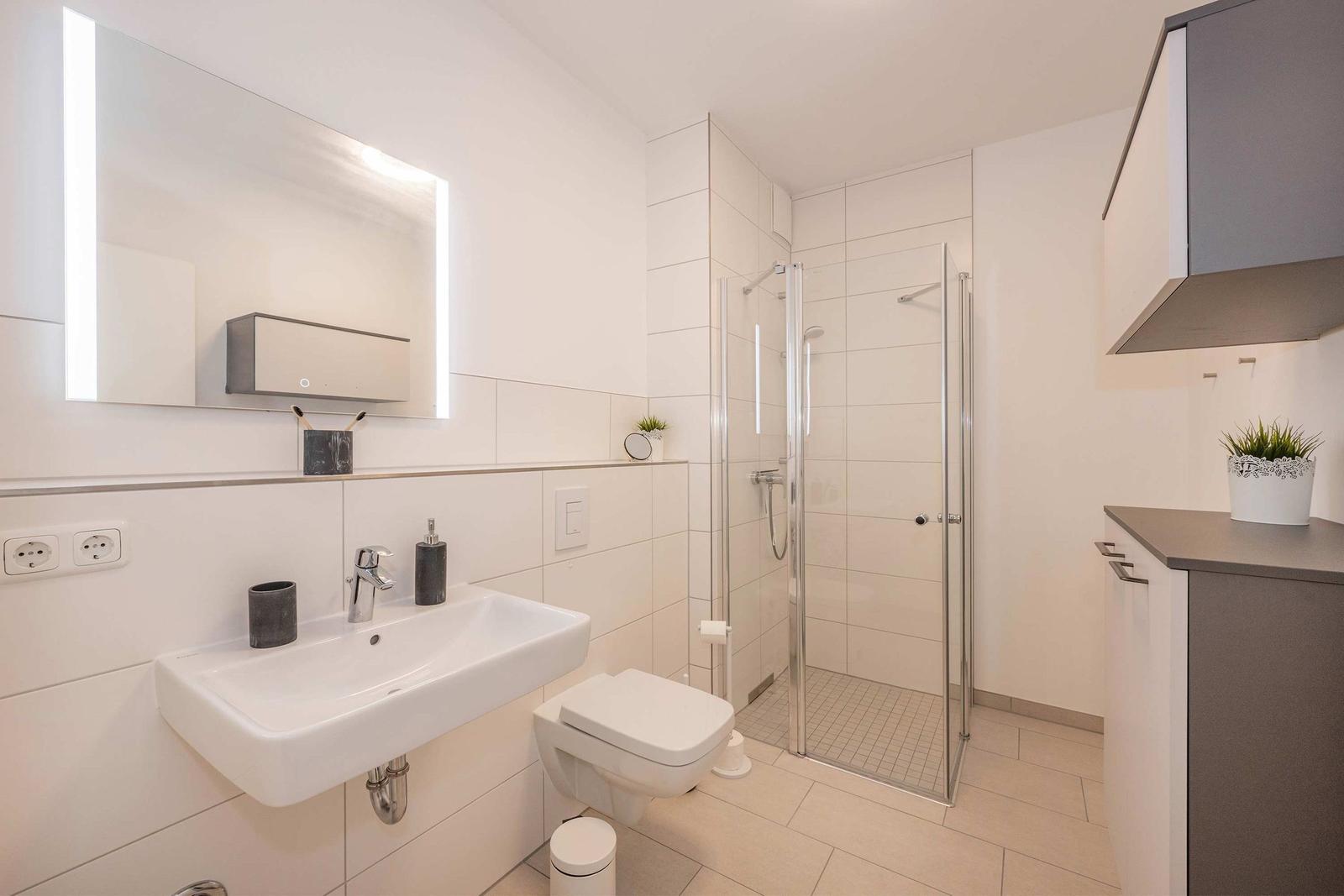 Badezimmer mit Dusche, Waschbecken und Toilette. Moderne Einrichtung mit Spiegelschrank.