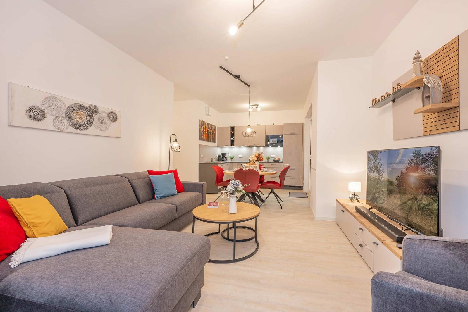 Wohnzimmer mit Sofa, Esstisch und Küche im Hintergrund.