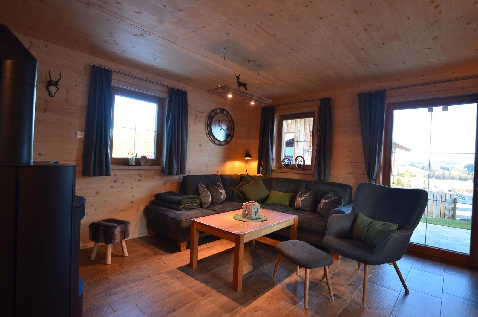 Wohnzimmer mit Holzwand, Sofa, Sessel und Tisch. Große Fenster und Tür mit Blick.