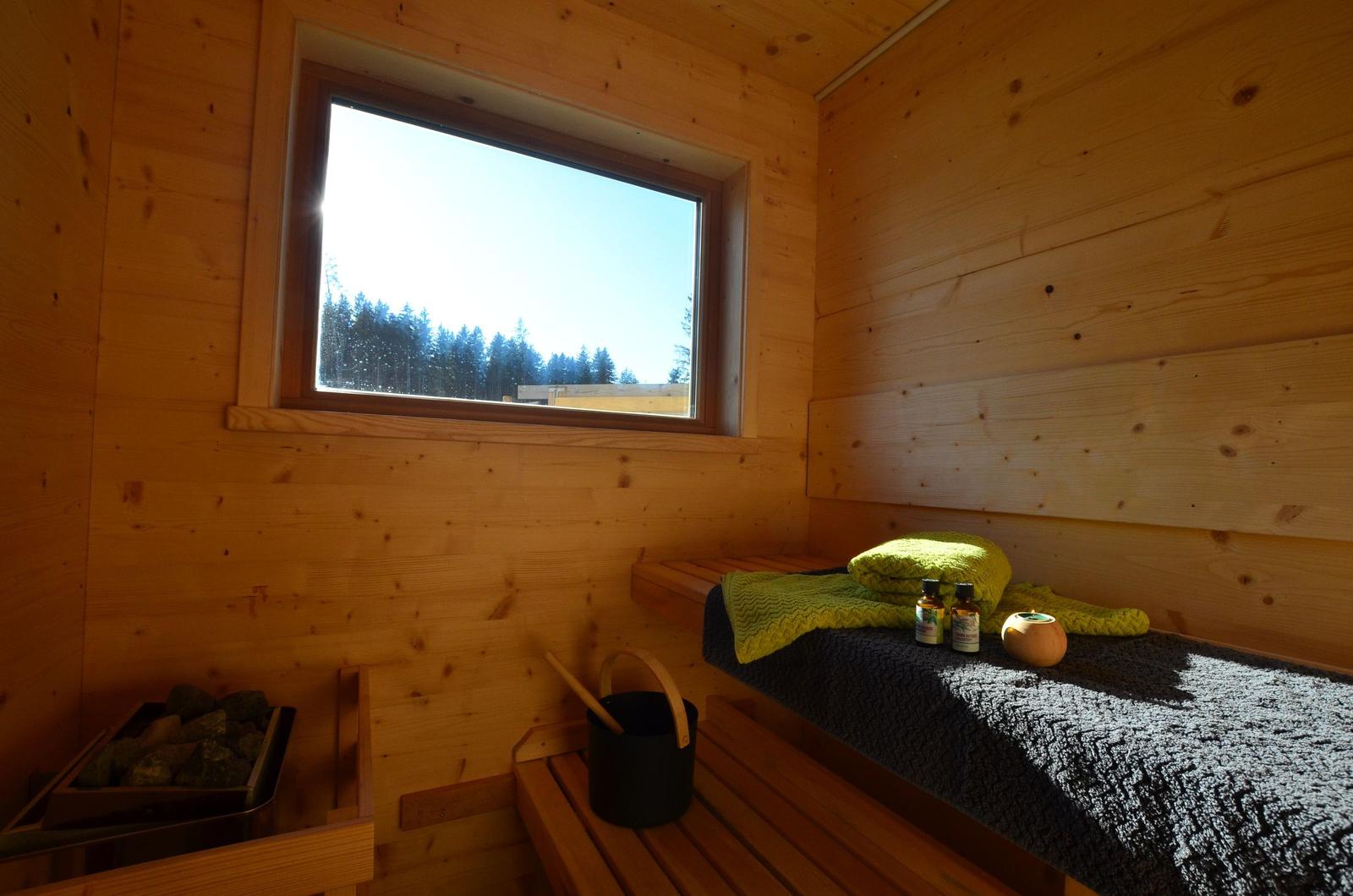 Sauna mit Holzwand, Fenster und Sitzbank mit Handtuch und Ölen.