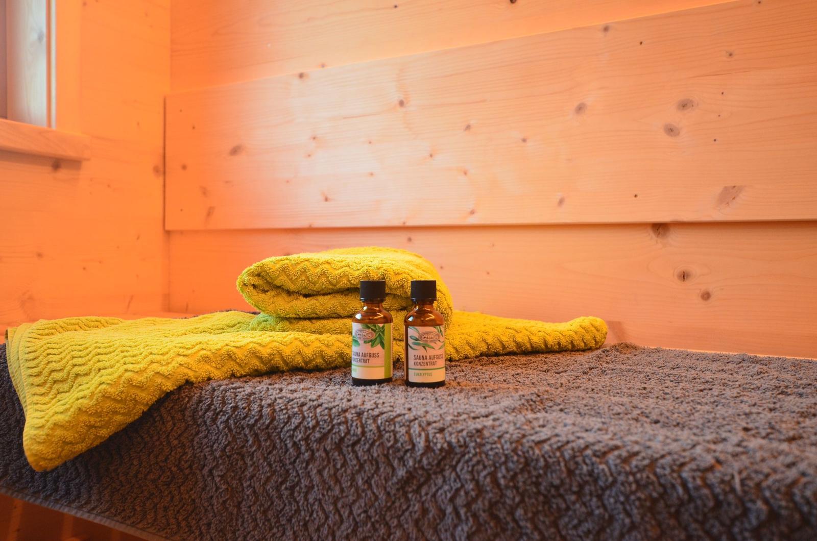 Sauna mit gelben Handtüchern und zwei Saunakonzentraten auf grauem Deckenbezug.