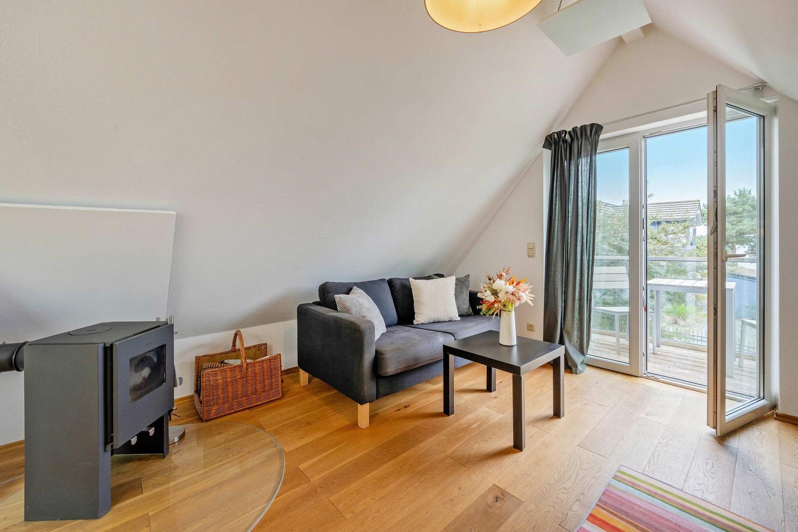 Wohnzimmer mit Sofa, Kamin und Balkontür. Holzboden und schräges Dach.
