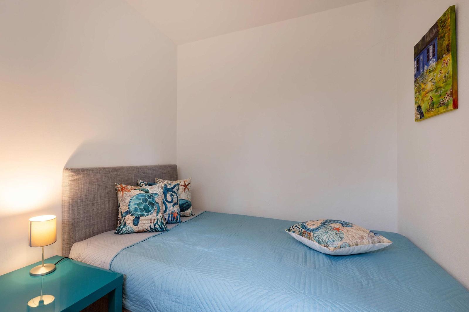 Ein Schlafzimmer mit Bett, Kissen und Nachttisch. An der Wand hängt ein Bild.