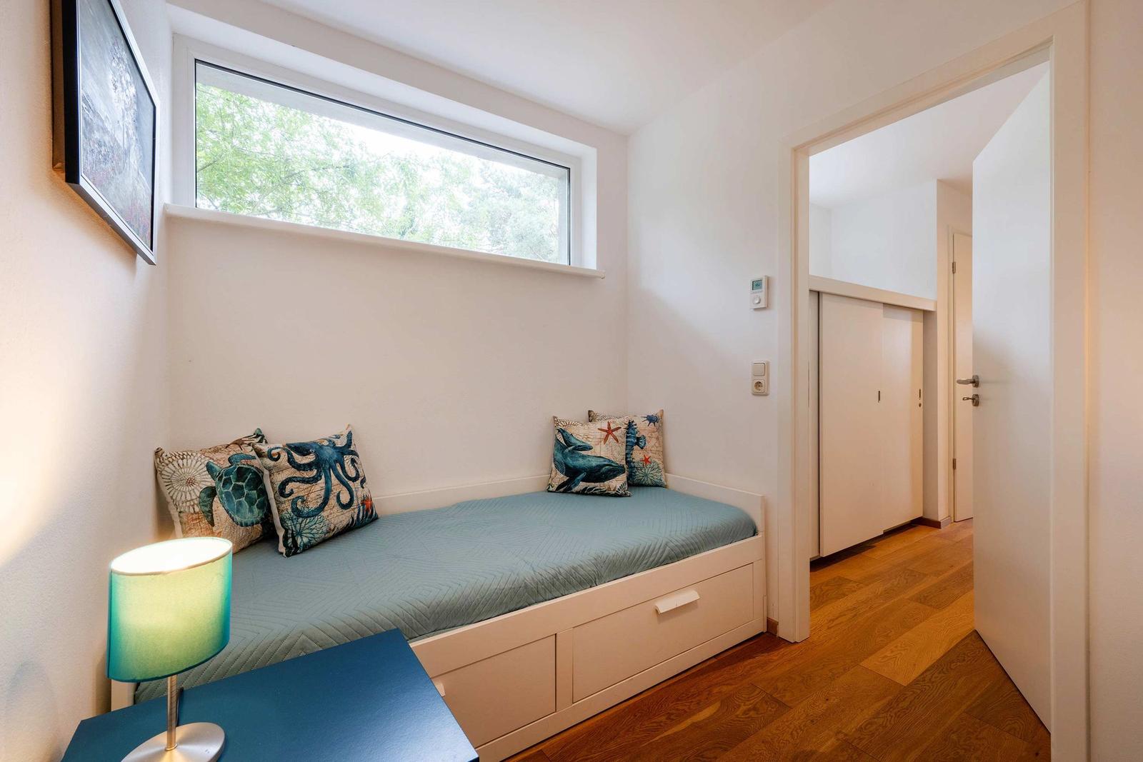 Schlafzimmer mit Fenster, Bett und Nachttisch. Holzfußboden und Kleiderschrank sichtbar.